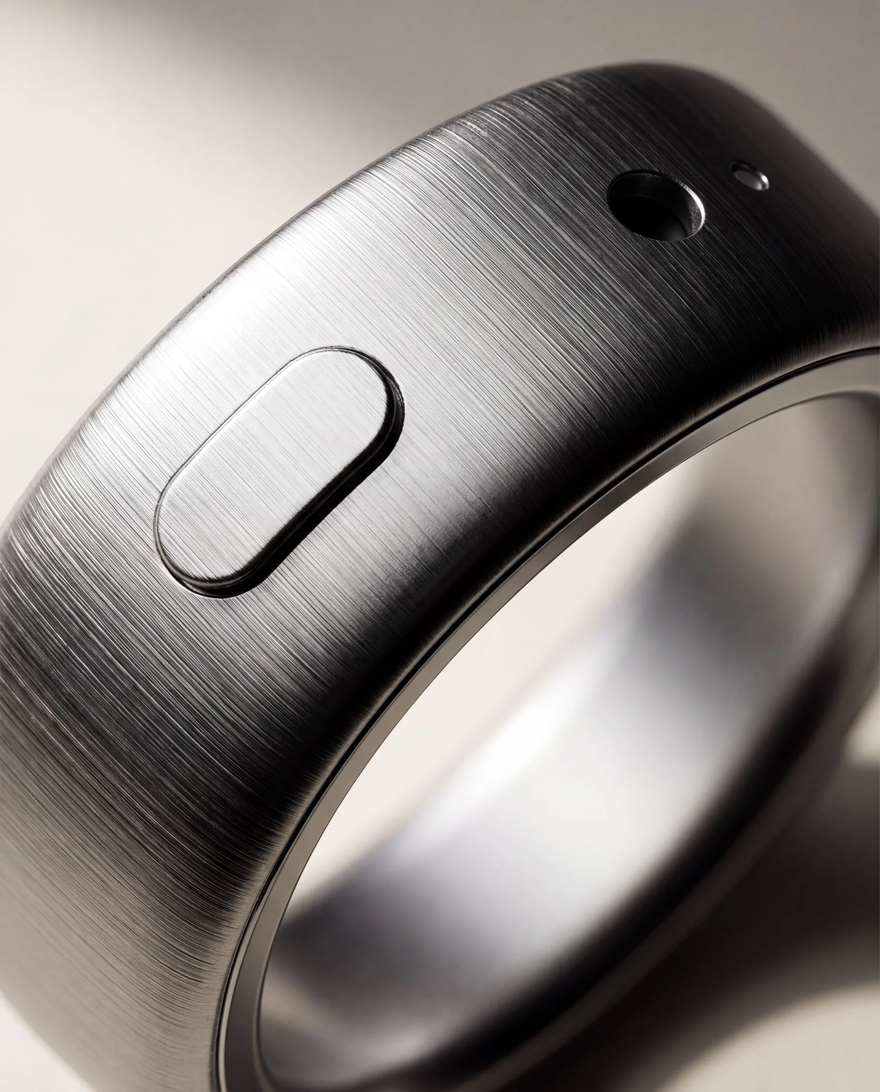 Extreme macro of the pill button standing proud of the brushed band, with the microphone port beyond